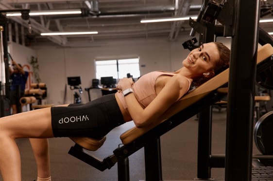 woman, sporting a Whoop fitness wearable on her wrist, reclines on workout equipment in gym